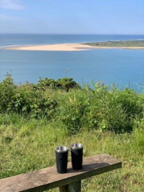 A bench with two metal cups in a natural setting with a view of a beach and ocean. - Fabulous apartment for 2 in Llansteffan (Llansteffan)
