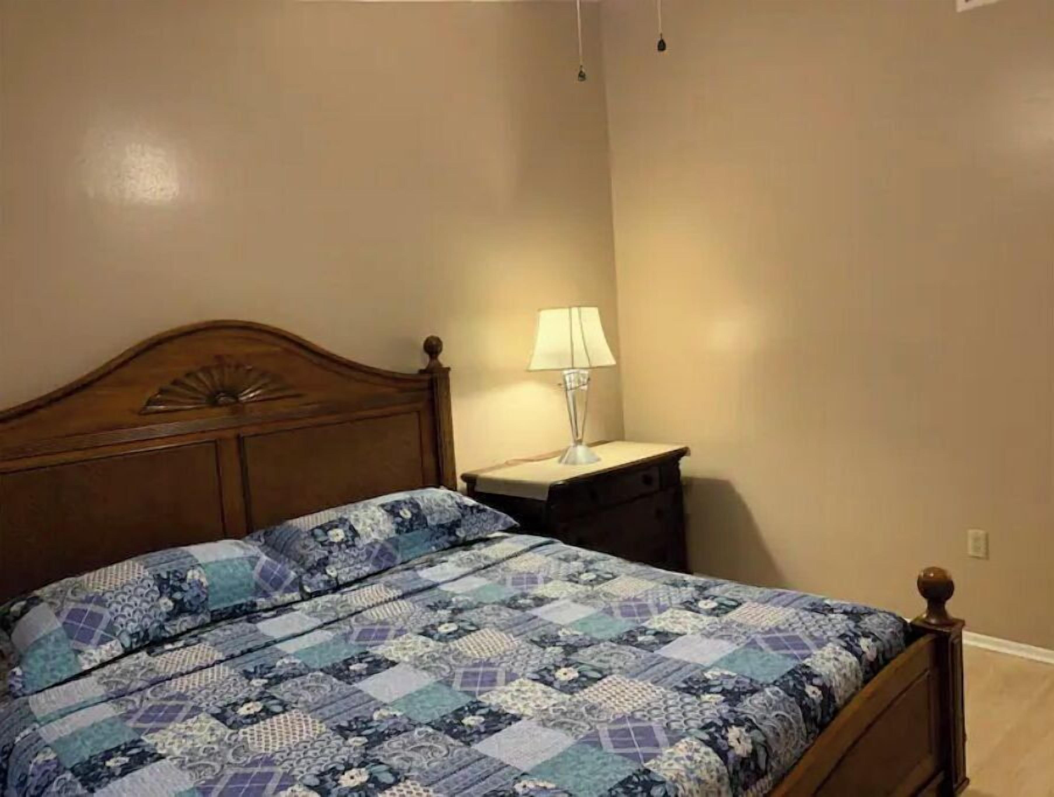 Ein Schlafzimmer mit einem hölzernen Bett, einem Nachttisch mit Lampe und einer schlichten Wand.
