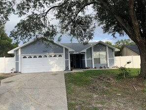 Stylish single-story home with a central entrance and two windows on each side, set behind a white fence in a suburban area.