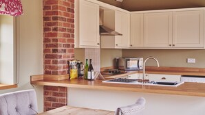 Una cocina con armarios blancos, pared de ladrillo, encimera de madera, lavamanos y lámpara colgante.