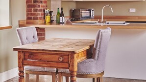 Una cocina con una mesa de madera, dos sillas, un muro de ladrillo, un microondas y lámparas colgantes.
