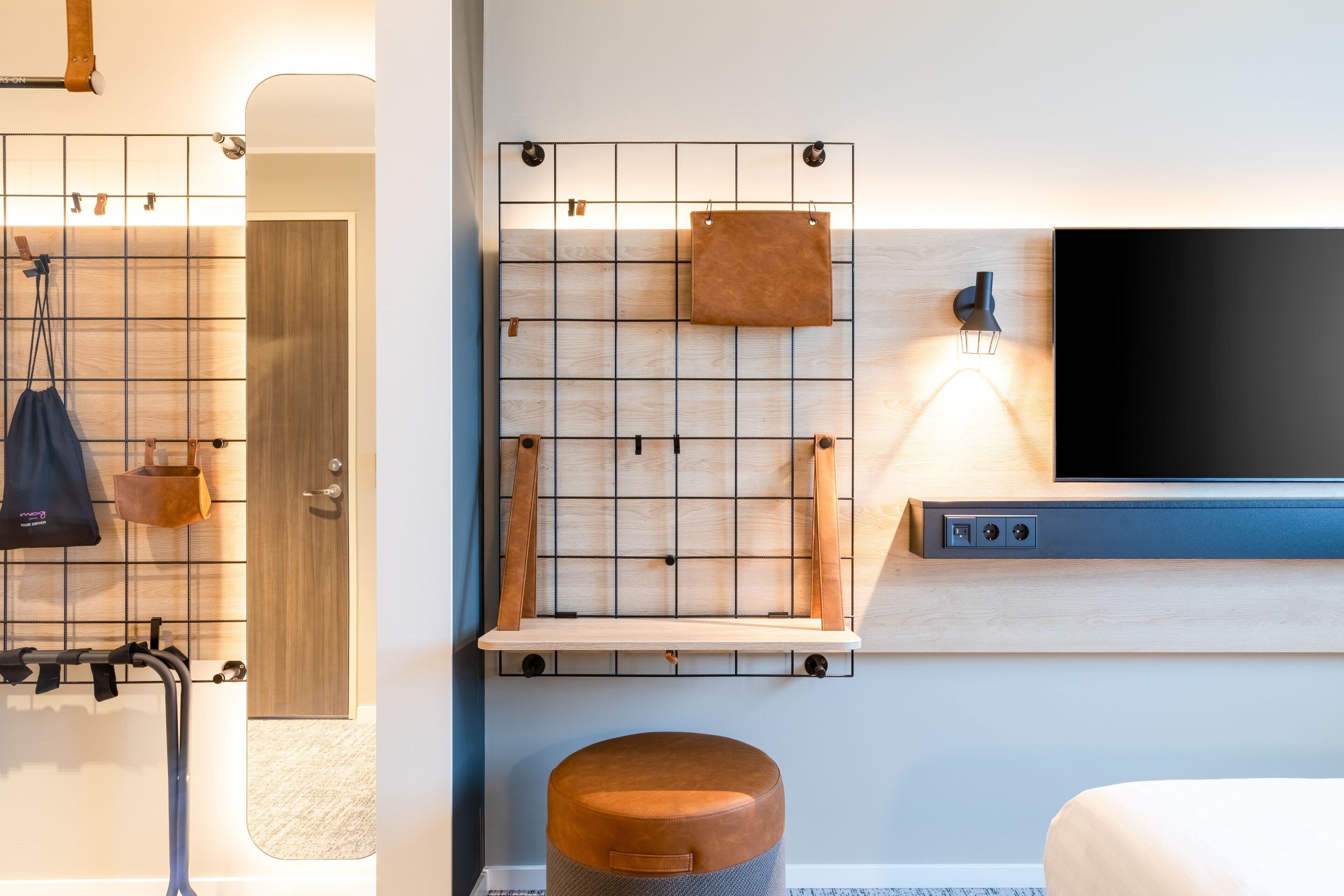 A modern hotel room with a wooden grid wall, a mounted TV, and a small wooden shelf.