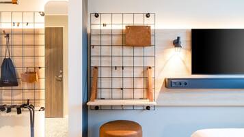 Habitación de hotel moderna con un panel de pared de madera, un televisor montado y un pequeño estante de madera.