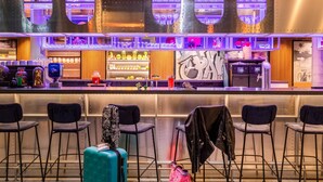 Zona de bar con mostrador, taburetes y estantes llenos de botellas y vasos.