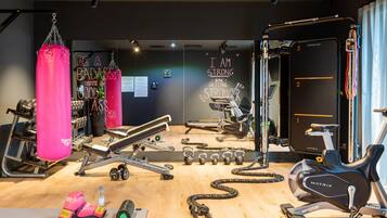 Ein Fitnessstudio mit verschiedenen Trainingsgeräten, darunter ein Schlagbeutel, Hanteln und ein Ergometer.