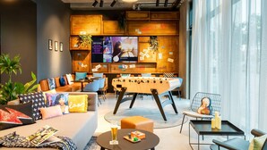 Un espacio lounge moderno con mesa de fútbol, asientos cómodos y una pantalla de televisión que muestra un video.
