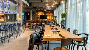 Um restaurante moderno com uma longa mesa de madeira, área de bar e grandes janelas.