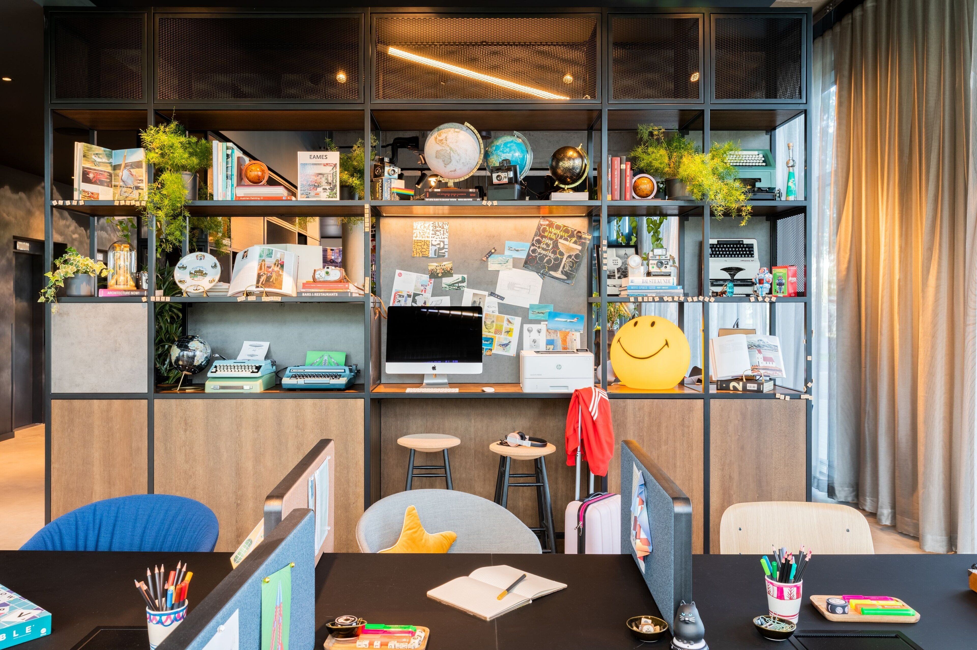 Un espacio de trabajo moderno con un escritorio, computadora y estanterías llenas de libros, globos y objetos decorativos.