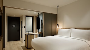 A modern hotel room with a large bed, a bedside table, a mirror, and a small desk area.