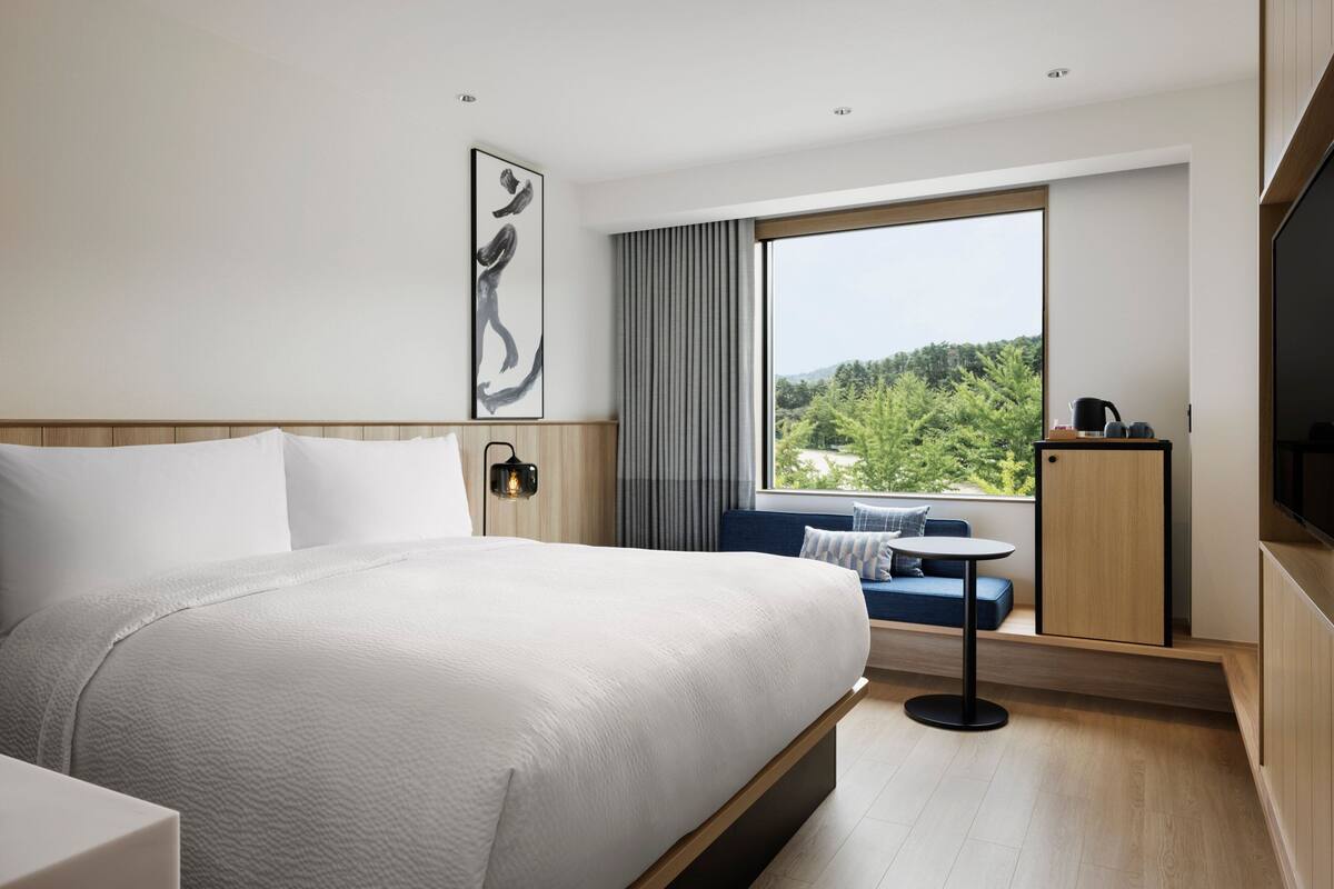 A modern hotel room with a large bed, a seating area with a view, and a TV.