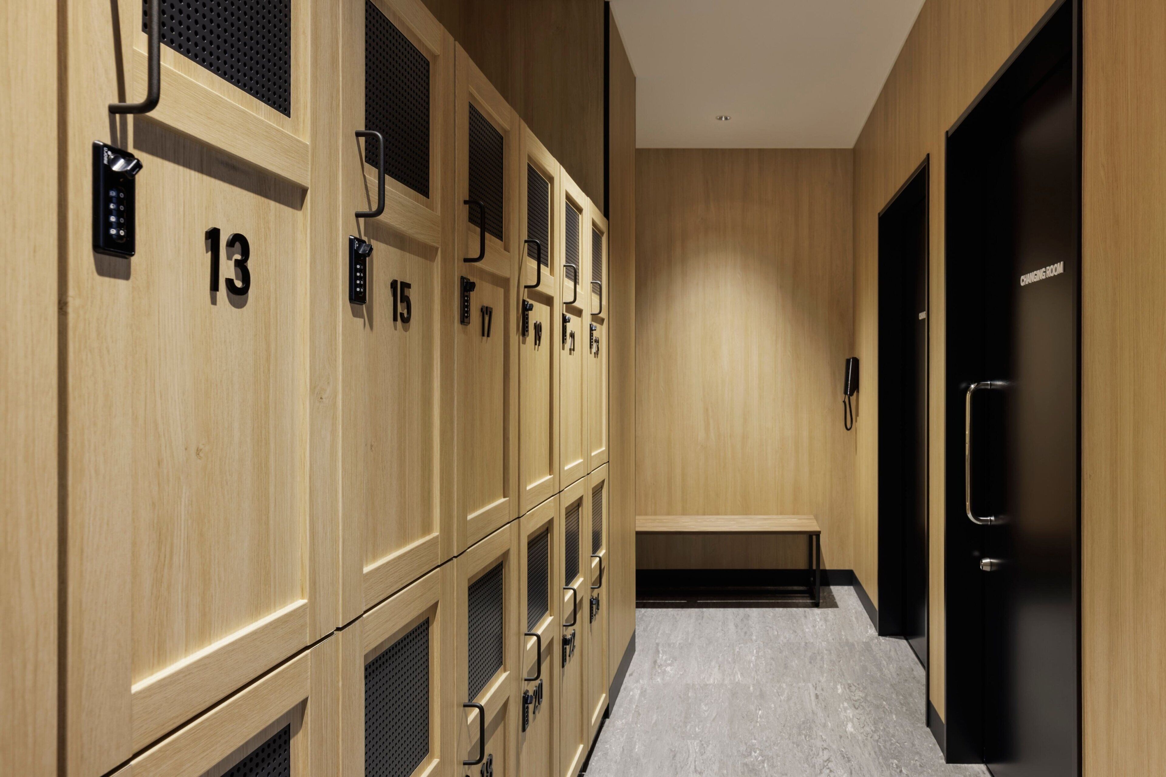 A row of wooden lockers with numbers 13 to 17, a bench, and a door with a sign.
