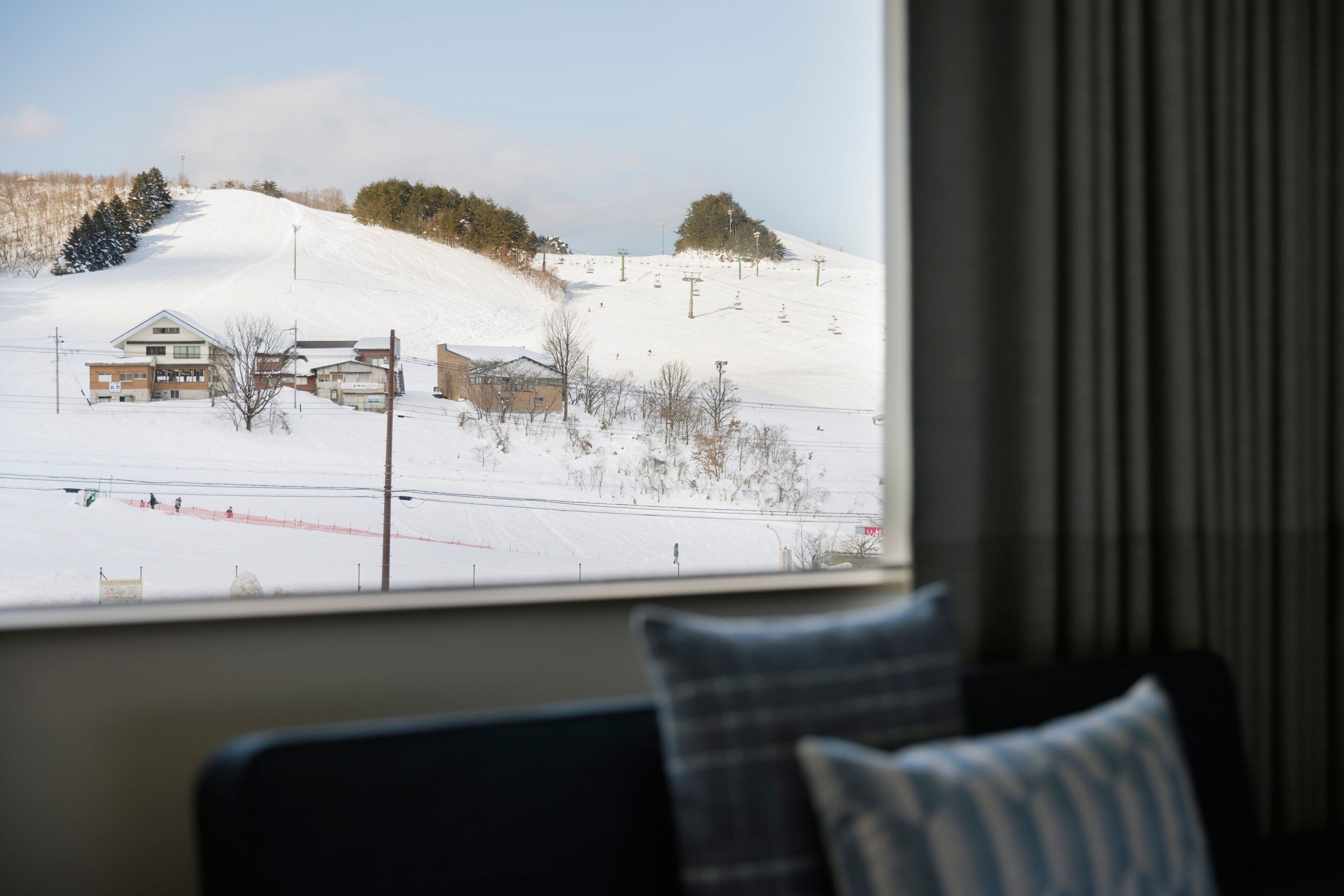 A view from a window of a hotel room with a snowy landscape outside, including a ski slope and buildings.
