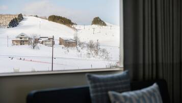 A view from a window of a hotel room with a snowy landscape outside, including a ski slope and buildings.