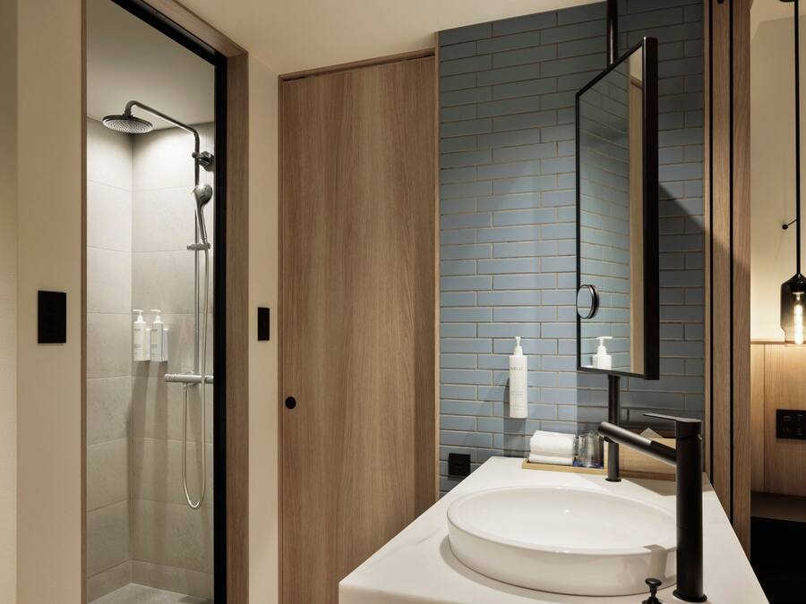 A modern bathroom with a glass shower enclosure, a wooden door, a sink with a black faucet, and a mirror above the sink.