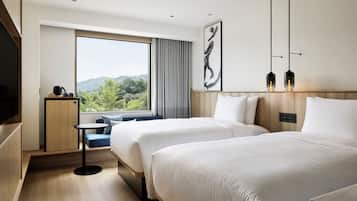 Habitación de hotel con dos camas, una mesita, televisión y ventana con vistas a zonas verdes.