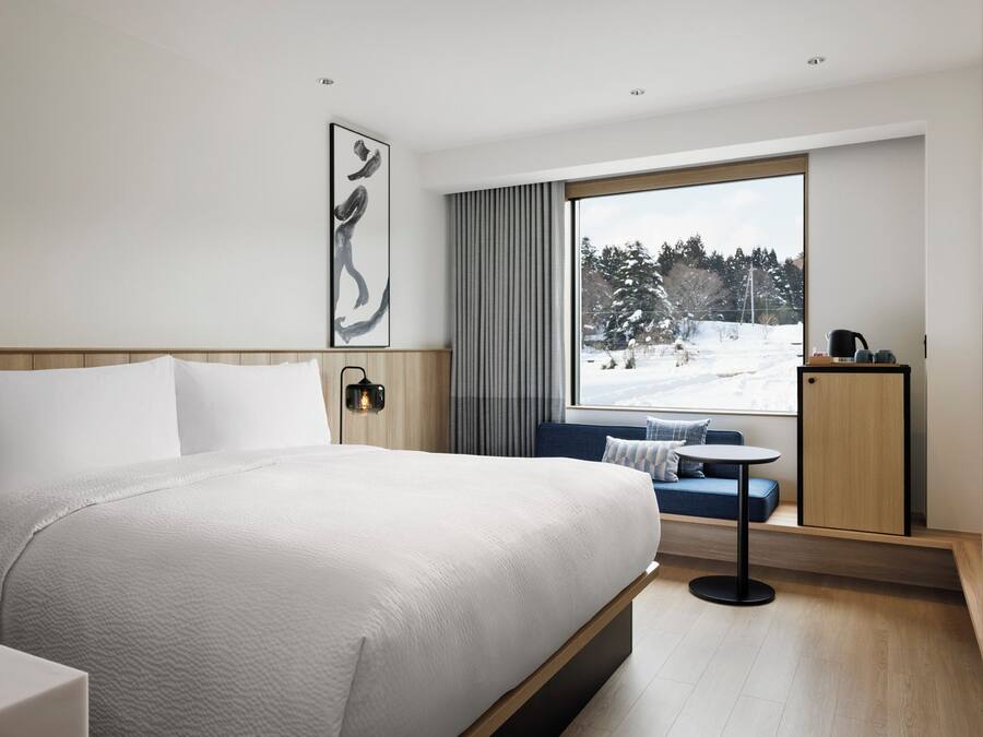 Ein Hotelzimmer mit einem großen Bett, einem Schreibtisch mit Stuhl, einem Fernseher und einem Fenster mit Blick auf eine verschneite Landschaft.
