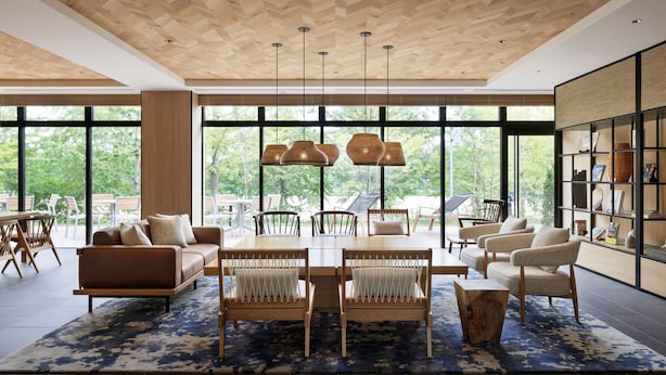 A modern living room with a large window, a wooden ceiling, and a dining area with chairs and a table.