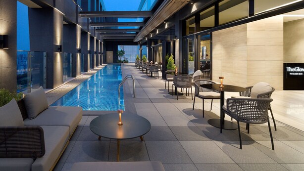 A modern outdoor pool area with a glass-enclosed pool, lounge seating, and a bar area.