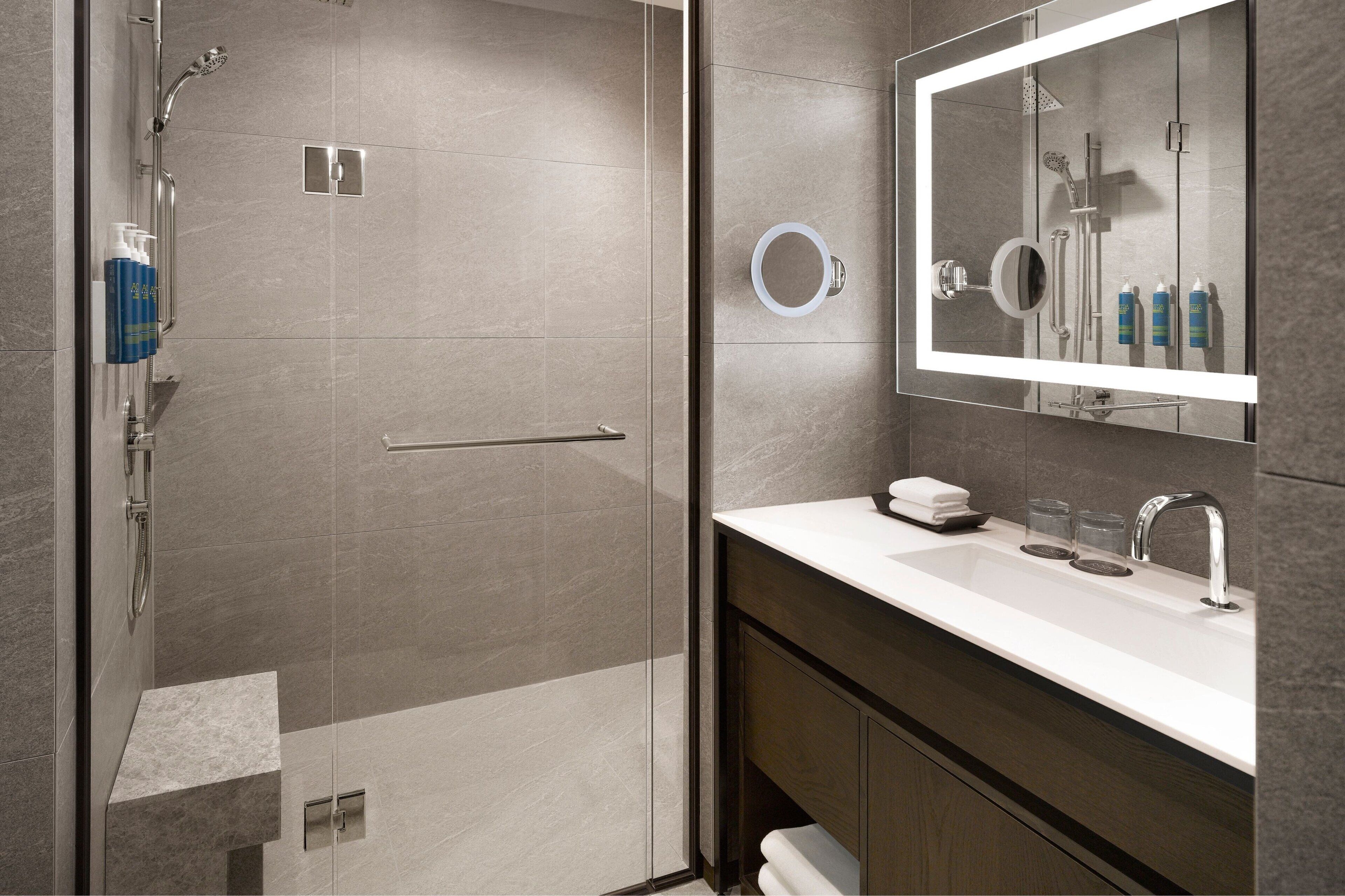 Une salle de bain moderne avec une douche à parois de verre, un lavabo blanc avec un miroir et des articles de toilette posés sur le comptoir.