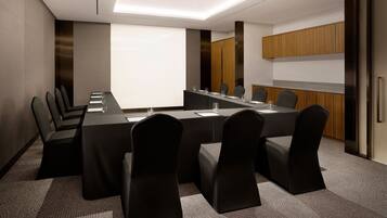 A conference room with a long table, chairs, a projector screen, and wooden cabinets.