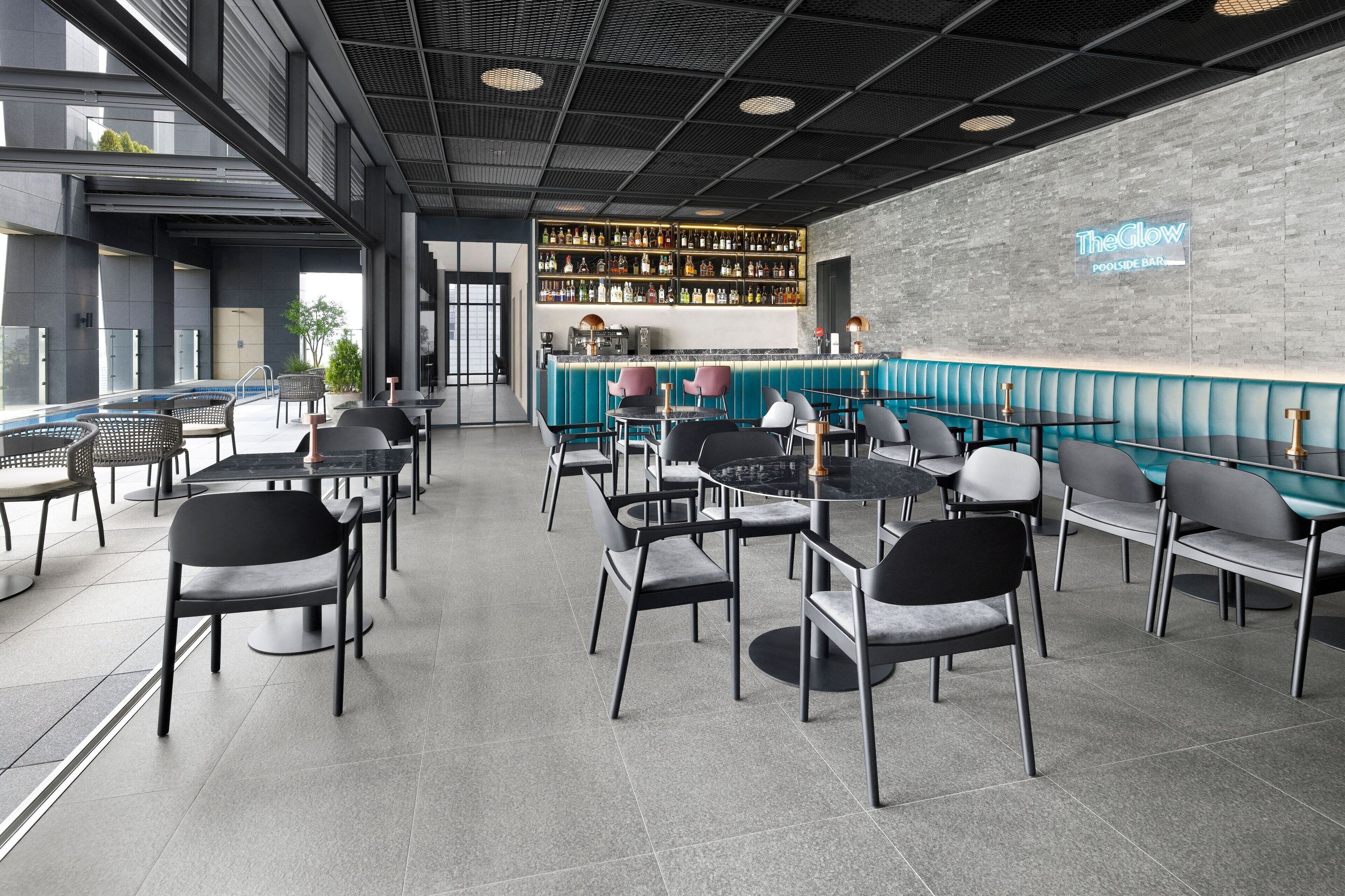 A modern bar area with a poolside seating arrangement, a bar counter with a variety of bottles, and a sign reading "The Glow Poolside Bar".