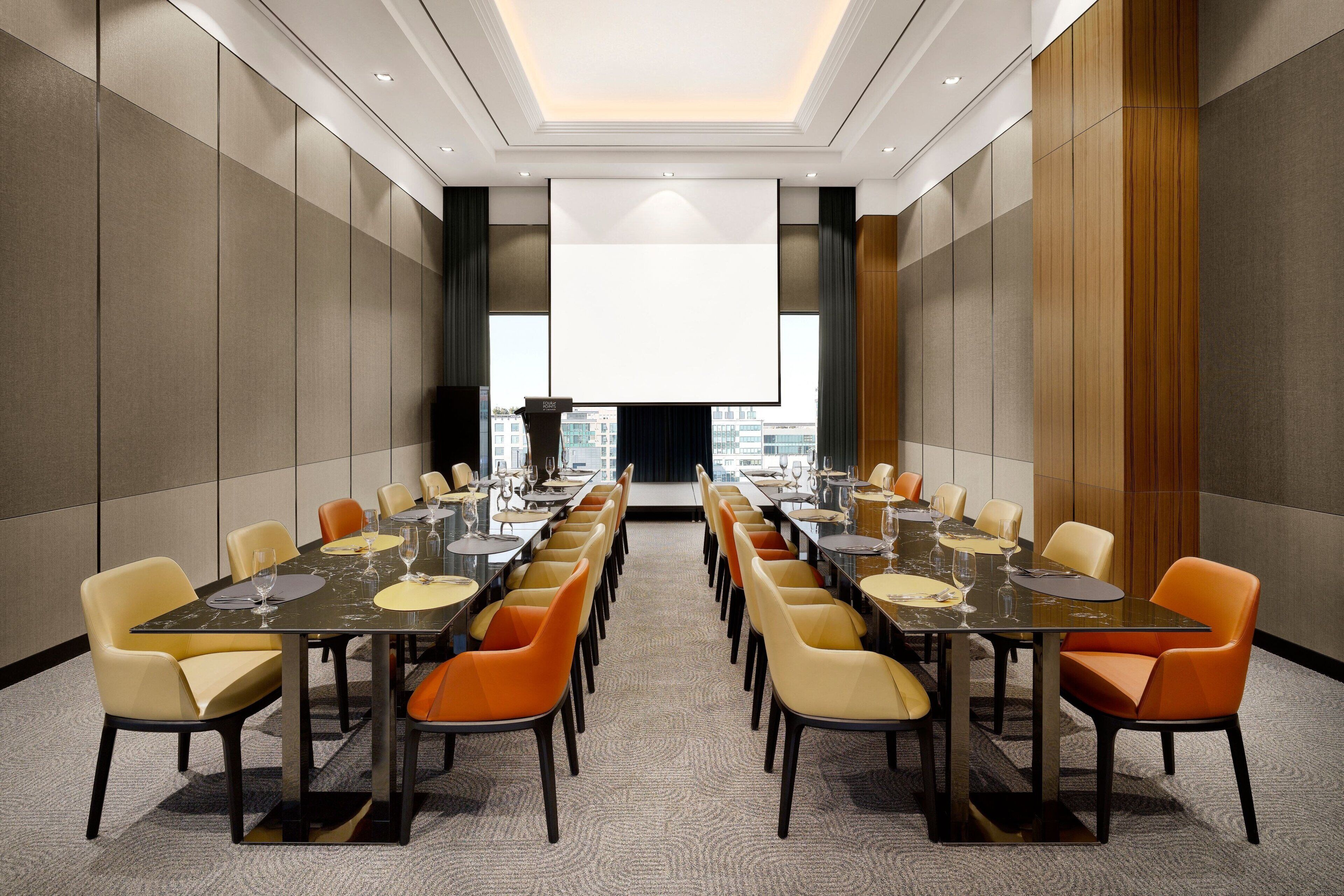 A conference room with a long table, multiple chairs, and a large screen at the front.