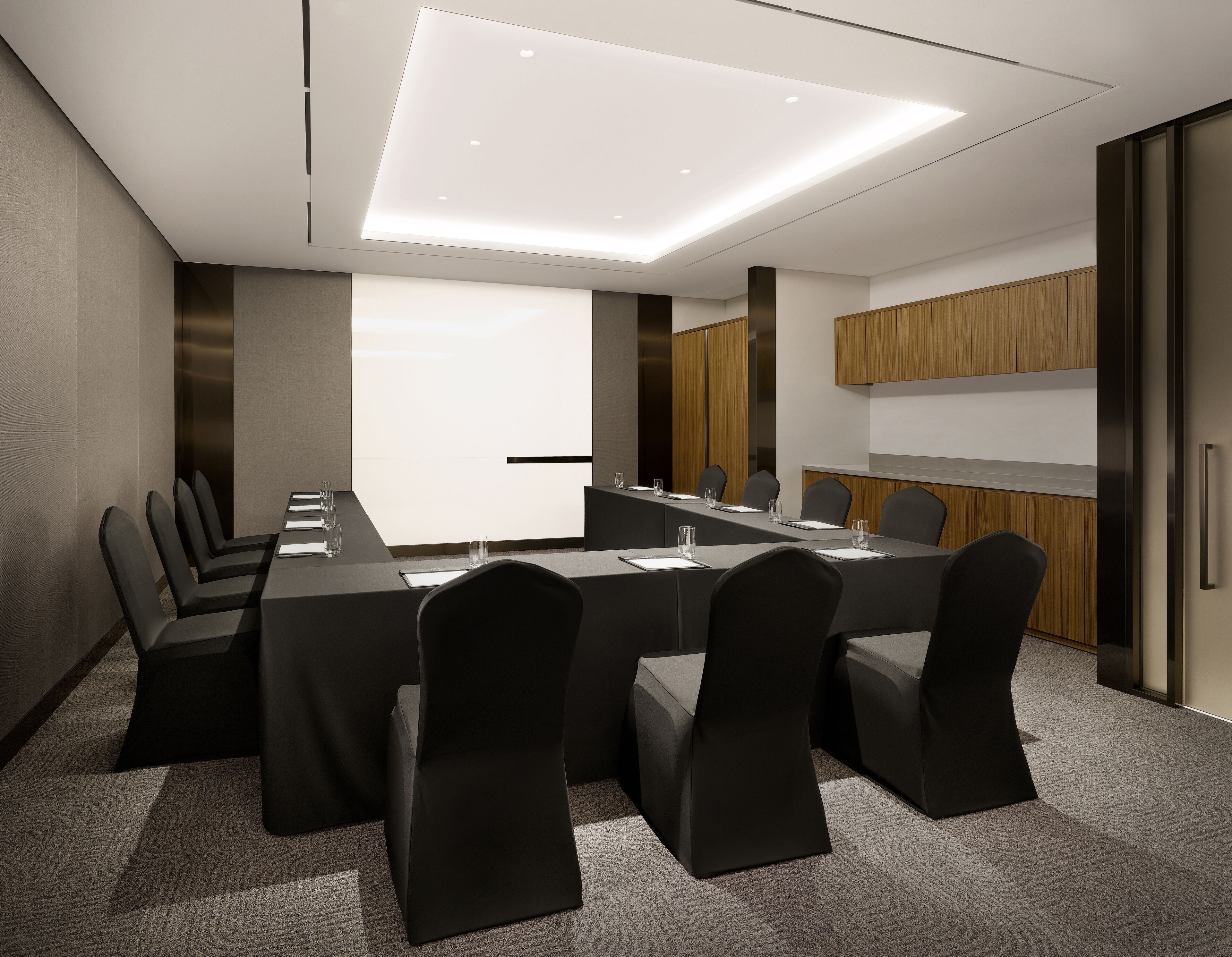 A conference room with a long table, chairs, a projector screen, and a wooden cabinet.