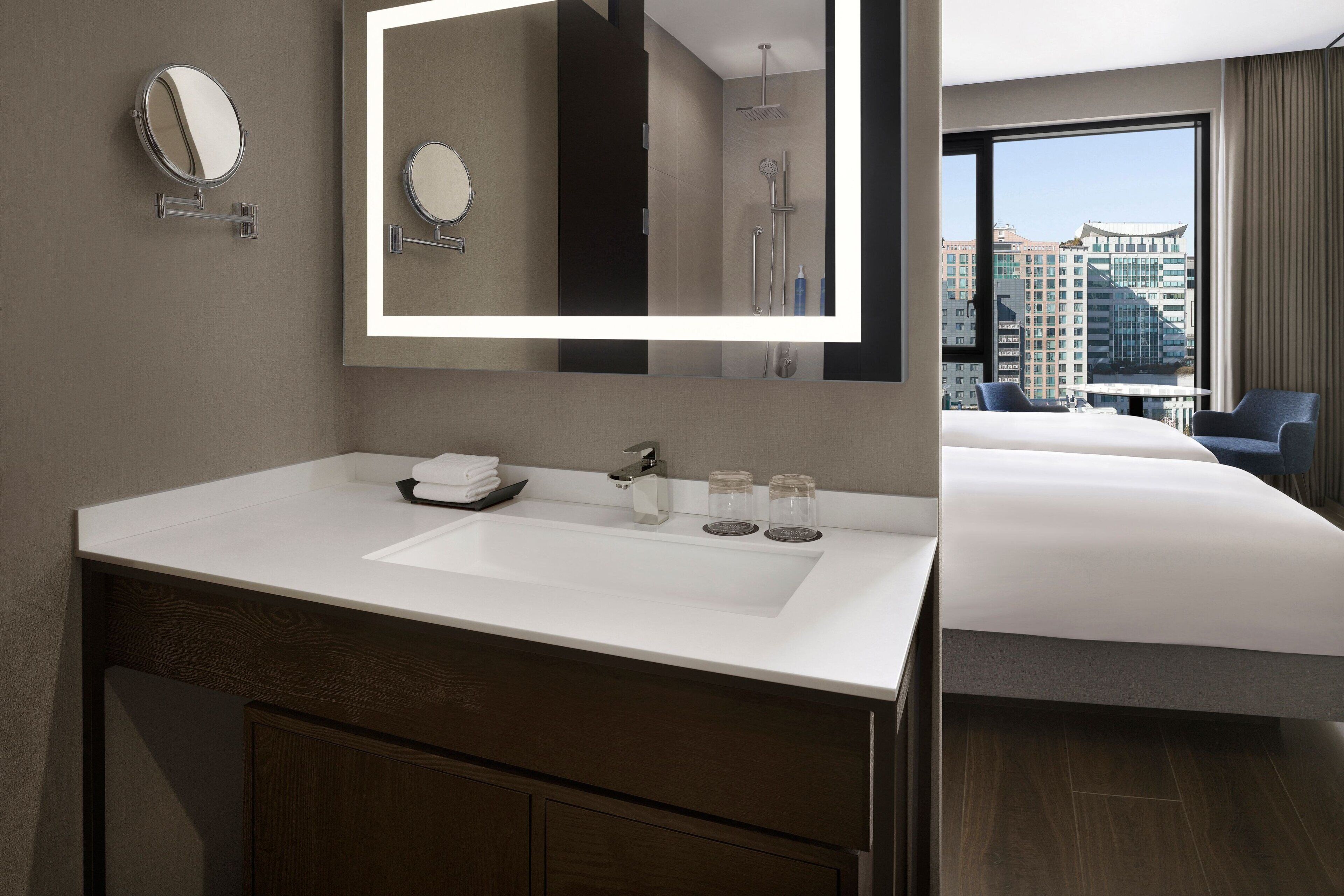 Un baño de hotel moderno con un espejo grande, un lavamanos blanco y una zona de ducha.