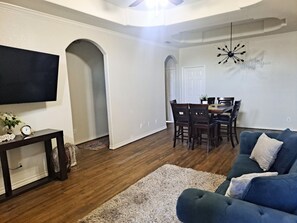 Ein Wohnzimmer mit Fernseher, Couchtisch, Sofa und einem Essbereich mit Stühlen und Tisch.
