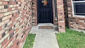 A brick house with a black front door, a small porch, and a window to the right. - Beautiful house close to the sea (Corpus Christi)