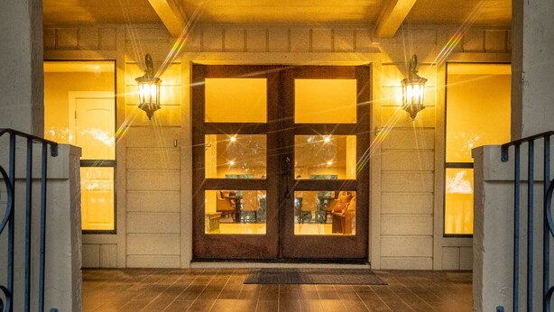 A hotel entrance with a wooden door, two wall-mounted lights, and a stone-paved entrance.