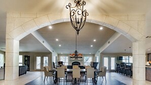 A spacious dining area with a high ceiling, stone arches, and a central chandelier.