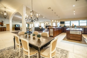 A spacious kitchen with a central island, a dining area with a large table and chairs, and a living area with sofas and a fireplace.