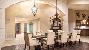 A dining area with a large table and multiple chairs, an arched ceiling, and a chandelier.