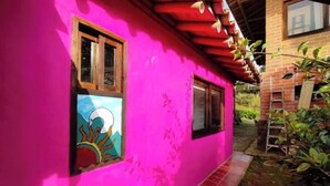 A pink house with a tiled pathway leading to a wooden door. - Bird Cabin (Antioquia)