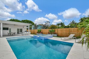 A swimming pool with a tiled deck, a covered patio area, and a wooden fence.