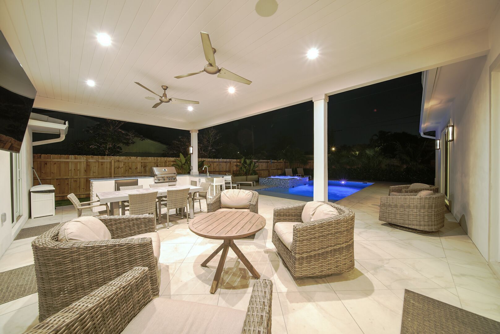 An outdoor patio with wicker furniture, a round table, ceiling fans, and a pool.