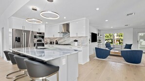 A modern kitchen with a large island, stainless steel appliances, and a dining area with blue chairs. - 18 Managed By Brampton Park (Delray Beach)