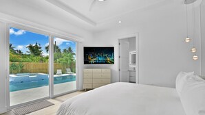 A bedroom with a large bed, a TV mounted on the wall, and a sliding glass door leading to a pool area. - 18 Managed By Brampton Park (Delray Beach)