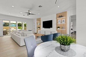 A modern living room with a white sofa, blue chairs, a marble table, and a TV mounted on the wall.
