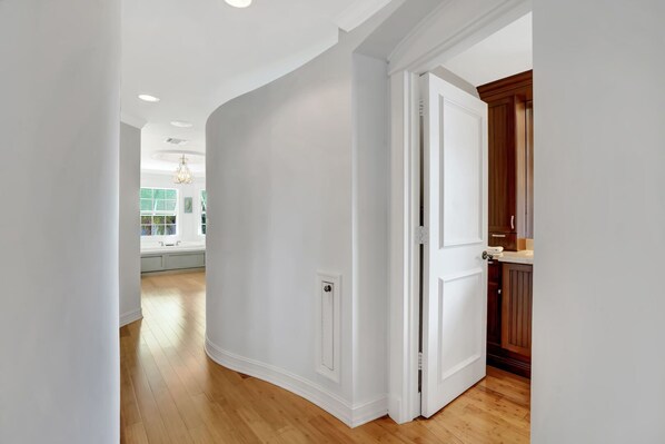 Un pasillo con paredes blancas, suelo de madera y una puerta entreabierta que da a una zona de cocina.