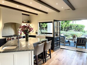 A modern kitchen with a marble countertop, a built-in stove, and a large window overlooking a garden. - Montecito - Ocean and Mountain Views - Total Renovation Completed! (Montecito)