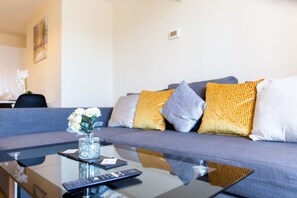 Un salón moderno con un sofá gris, una mesa de centro de cristal y un jarrón con flores blancas.