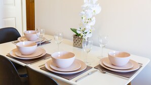 Une table à manger dressée avec des bols, des assiettes et des couverts blancs, accompagnée de verres à vin et d’un vase contenant des fleurs blanches.