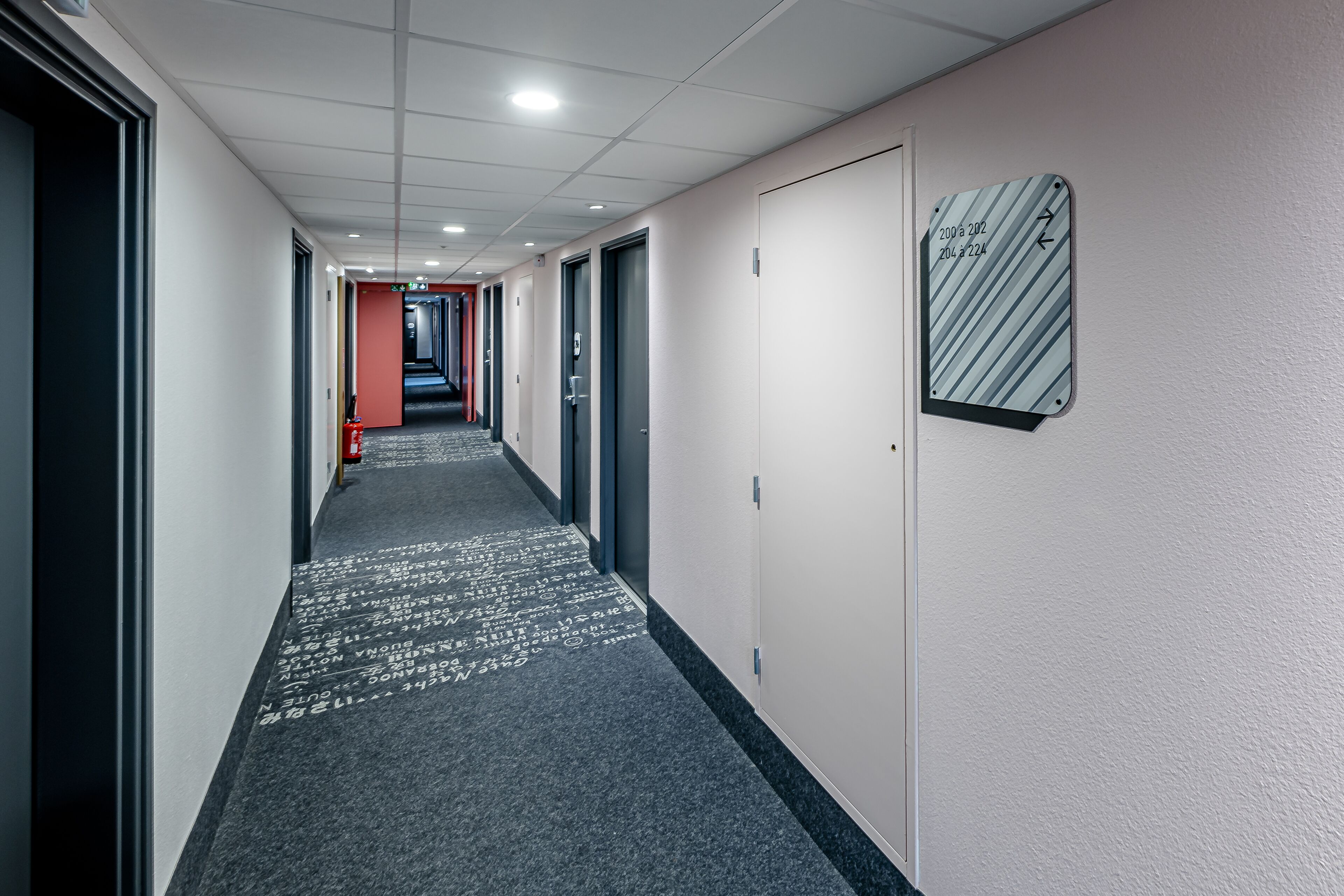 A hotel corridor with a carpeted floor, doors, and a fire extinguisher.