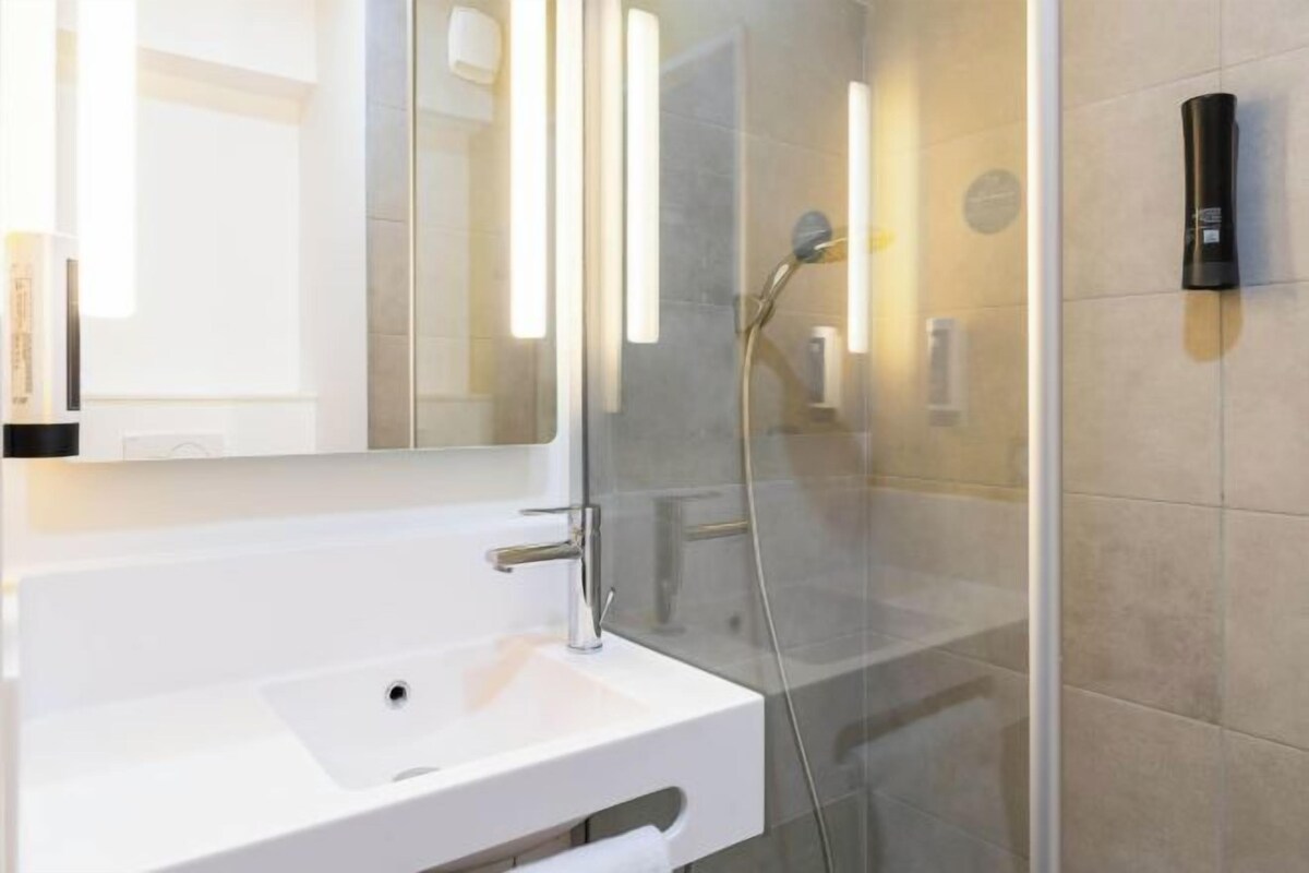 A modern bathroom with a glass-enclosed shower, a white sink, and a large mirror.