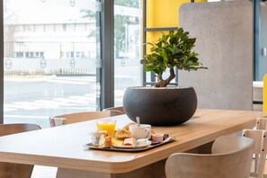 Ein Esstisch mit Topfpflanze, einer Kaffeetasse, einem Orangensaftglas und Gebäck.