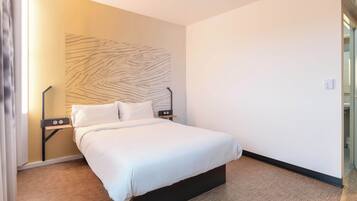 Une chambre d’hôtel moderne avec un grand lit, une table de chevet, une lampe fixée au mur et un plancher en bois.