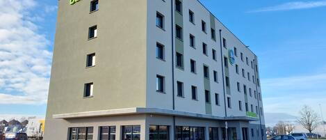 A B&B hotel with a modern design, featuring a flat facade, multiple windows, and a parking area with marked spaces.