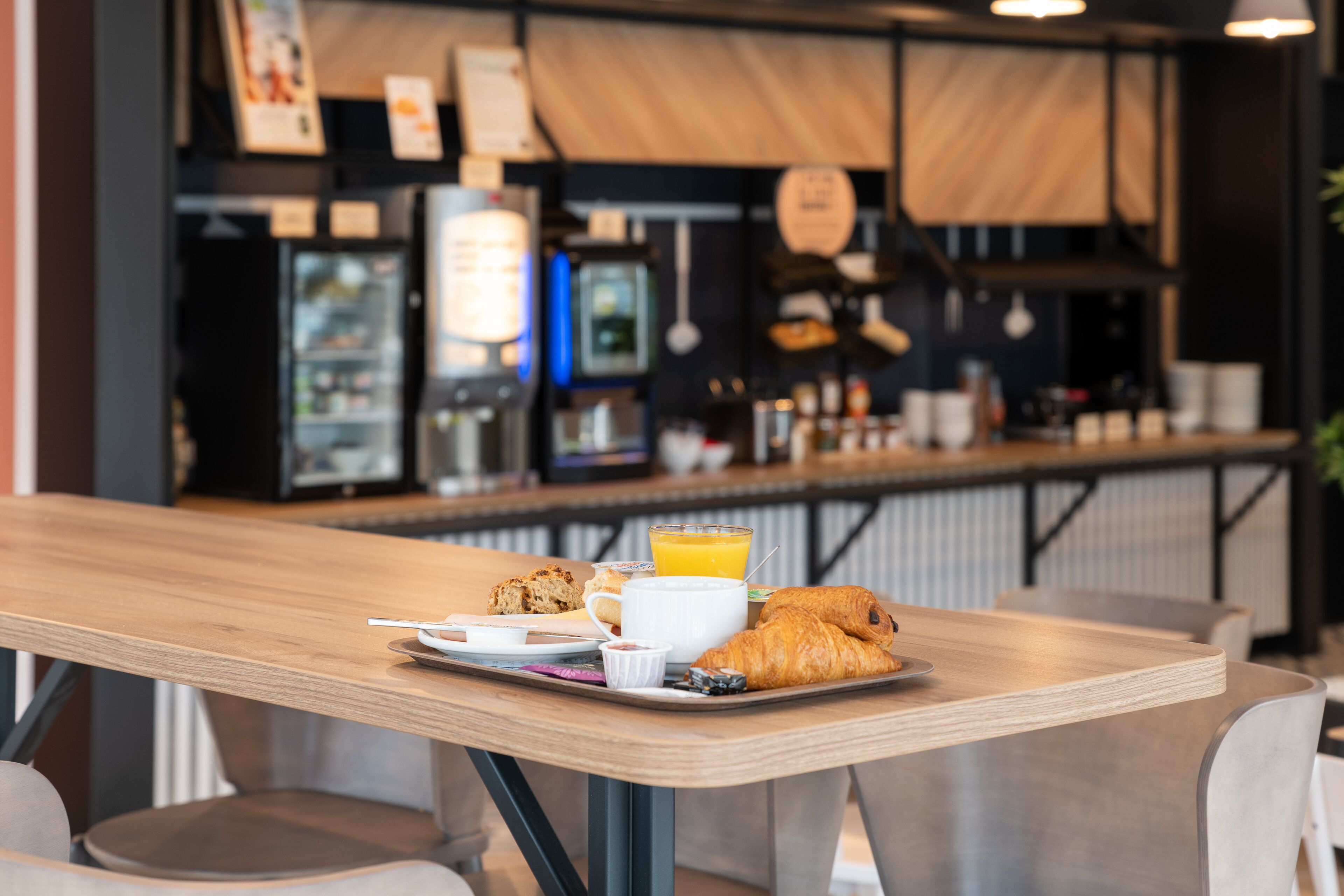 A breakfast tray with croissants, a cup of coffee, and a glass of orange juice on a wooden table in a cafe setting.